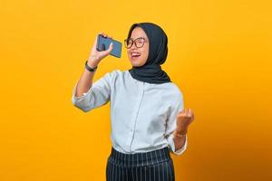 gelukkige jonge aziatische vrouw die geniet van zingen met smartphone op gele achtergrond