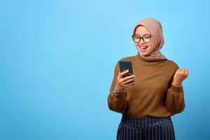 gelukkige jonge aziatische vrouw die mobiele telefoon met handgebaarsucces op blauwe achtergrond gebruikt foto