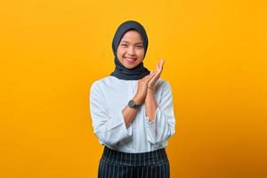 vrolijke mooie aziatische vrouw wrijft over haar handpalmen en glimlacht breeduit op gele achtergrond foto