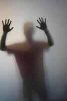 Mens met verheven handen silhouet achter berijpt glas foto