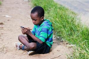 kind zittend op de grond met mobiele telefoon in de hand. foto