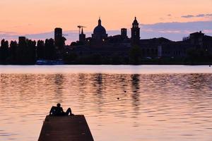 paar zittend op de pier kijkend naar de zonsondergang en de skyline van de stad foto