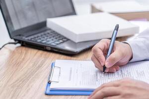 een Mens van auto onderhoud centrum schrijven Aan de klembord papier controleren onderhoud lijst in kantoor met nieuw lucht filter van auto koeling systeem en laptop computer Aan hout tafel foto