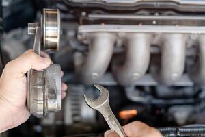 moersleutel in de hand- van een technicus voor nemen uit riem spanning katrol oud een deel auto motor vervanging van Reserve onderdelen in motor kamer foto