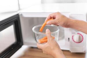 dichtbij omhoog hand- een Mens zetten glas kom met krab stokjes in magnetronoven oven naar koken in de keuken foto