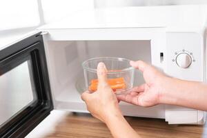 dichtbij omhoog hand- een Mens zetten glas kom met krab stokjes in magnetronoven oven naar koken in de keuken foto