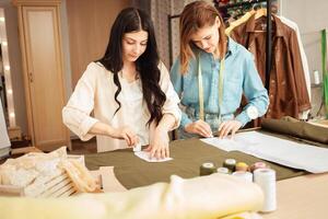 naaisters maken schetsen, patroon Aan kleding stof. atelier, maatwerk van individu kleren, klein bedrijf. werkwijze van werk in werkplek. foto