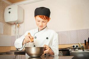 roodharig jongen in chef-kok kostuum kookt pannekoeken in keuken, kneedt deeg, assistent maakt ontbijt. ritme deeg met vliegenmepper foto