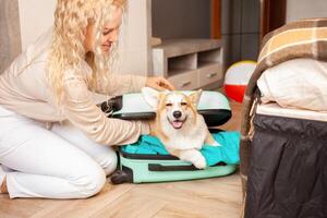 vrouw zet corgi hond, pup, in koffer. voorbereiding voor reis, aankomst Bij hotel, avontuur, tour, toerisme. liefde en zorg voor huisdieren, vervoer van dieren. lachend. foto