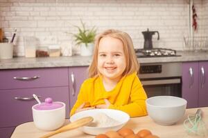 drie jaar oud meisje in geel jasje is voorbereidingen treffen naar koken voedsel in keuken. portret van gelukkig kind. glimlacht en looks in camera. foto