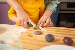 moeder en dochter koken taart in Purper keuken, opleiding en ontwikkeling, interessant spel en helpen. gelukkig familie samen. besnoeiing pruimen. foto