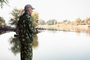 oudste Aan bank van rivier, een Mens met een visvangst hengel vissen, mooi natuur, herfst. een oud Mens rust en liefdes zijn hobby. actief gezond levensstijl, buitenshuis. senior concept foto