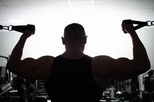 portret van een atleet, een sport- Mens trainer doet een oefening Aan simulator in de Sportschool. gezond actief levensstijl, schudt spieren. silhouet foto