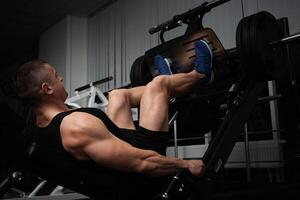 portret van een knap mannetje trainer in Sportschool. de atleet doet een oefening Aan de simulator in de Sportschool. bouwt spier, Toneelstukken sport, een gezond levensstijl. knijpt gewicht met poten foto