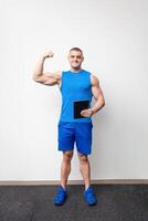 knap jong trainer in een sport- uniform met groot spieren met tablet Aan een wit achtergrond. glimlachen foto