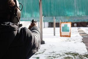 een Mens met hoofdtelefoons is het richten Bij de doelwit. een Mens in een scheutje branden een pistool. sport- vermaak uit de deur. foto