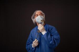 een mannetje dokter met een vreselijk oud injectiespuit in zijn handen. de dokter in een medisch masker, hoed, gewaad en handschoenen. een verschrikkelijk. de dokter bang maken met een reusachtig injectiespuit met een dik naald. foto