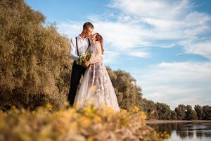 een jong bruiloft paar in liefde Aan de rand van een klif tegen de backdrop van de rivier- en de lucht. een vrouw in een mooi grijs jurk, een Mens in een pak Aan de kust van de meer. foto