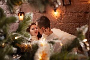 een vent met een meisje is vieren kerstmis. een liefhebbend paar geniet elk andere Aan nieuw jaar liefde verhaal. Kerstmis decoraties in de foto studio poseren voor modellen