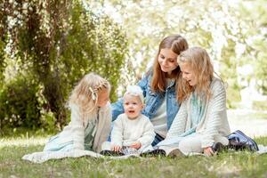 moeder met drie dochters zit Aan een picknick in de zomer en looks Bij hen met liefde foto