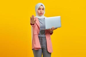 portret van een mooie aziatische vrouw die een laptop vasthoudt met open armen die een stopbord doet met een serieuze en zelfverzekerde uitdrukking foto