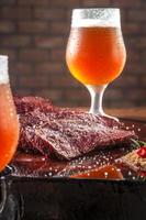 gegrilde denver steak gesneden op houten snijplank met parrillazout en twee zweterige kluit glazen bier. marmeren vlees rundvlees - close-up. foto