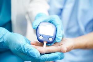 Aziatisch dokter gebruik makend van digitaal glucose meter voor controleren monster bloed suiker niveau naar behandeling suikerziekte. foto