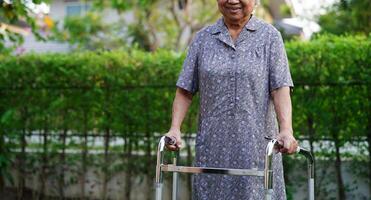Aziatische bejaarde vrouw handicap patiënt lopen met rollator in park, medisch concept. foto