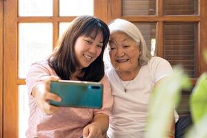 liefhebbend dochter nemen selfie gebruik makend van mobiel telefoon met moeder Bij huis. Japans familie. foto