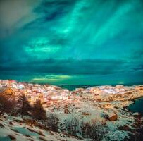 Aurora borealis gloeiend over- Scandinavisch dorp Aan kustlijn in winter Bij lofoten eilanden, foto