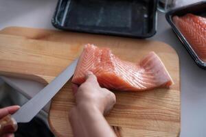 hand chef-kok met behulp van mes plak rauwe zalm op snijplank foto