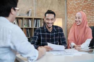 twee jonge startup-collega's die islamitische mensen zijn, praten over financiële projecten met een klant met een glimlach, presentatiesucces met een zakelijke grafiek op het bureau van een kleine kantoorwerkplek. foto