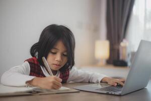 schattig en gelukkig weinig Aziatisch meisje kinderen gebruik makend van een laptop computer, aan het studeren door een online e-learning systeem Bij huis. foto