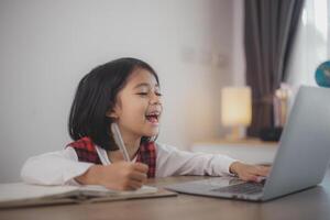 schattig en gelukkig weinig Aziatisch meisje kinderen gebruik makend van een laptop computer, aan het studeren door een online e-learning systeem Bij huis. foto