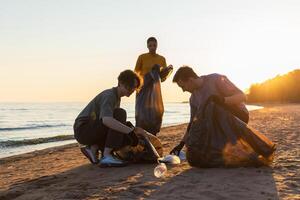 aarde dag. vrijwilligers activisten verzamelt vuilnis schoonmaak van strand kust- zone. vrouw en mans zet plastic uitschot in vuilnis zak Aan oceaan oever. milieu behoud kust- zone schoonmaak foto