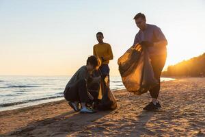 aarde dag. vrijwilligers activisten verzamelt vuilnis schoonmaak van strand kust- zone. vrouw en mans zet plastic uitschot in vuilnis zak Aan oceaan oever. milieu behoud kust- zone schoonmaak foto