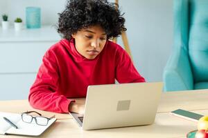 Afrikaanse Amerikaans meisje gebruik makend van laptop Bij huis kantoor op zoek Bij scherm typen chatten lezing schrijven e-mail. jong vrouw hebben virtueel vergadering online babbelen video telefoontje conferentie. werk aan het leren van huis foto