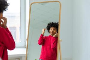 liefde jezelf. mooi jong glimlachen Afrikaanse Amerikaans vrouw dansen aanraken gekruld haar- genieten van haar spiegel reflectie. zwart dame op zoek Bij spiegel op zoek zelfverzekerd en gelukkig. zelf liefde concept foto