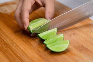 vrouw hand- Holding mes is snijdend limoen Aan een houten bord in keuken. snijdend vers citroen in stukken dichtbij omhoog. hoogte vitamine c natuurlijk foto