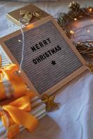 vilten letterbord vrolijk kerstfeest op het bed versierd met gouden krans, lichtjes en geschenkdozen