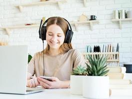 lachende tienermeisje in koptelefoon chatten met haar smartphone terwijl ze haar homewotk . doet foto