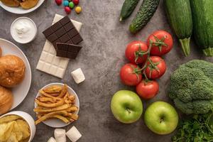 fruit en groenten versus snoep en frietjes bovenaanzicht plat op donkere achtergrond foto