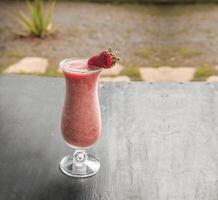 gezond aardbei smoothie in glas Aan donker hout. aardbei milkshake Aan donker hout met wazig achtergrond. detailopname heerlijk aardbei smoothie met aardbei stukken Aan hout. foto