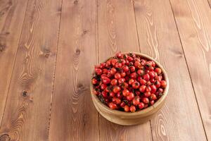 rood hondenroos rozenbottel fruit in een houten kom Aan houten tafel foto