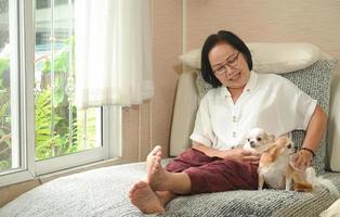 senior aziatische vrouw zittend met een hond op de bank, ze rustte en glimlachte. foto