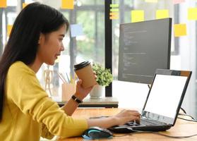 jonge professionele vrouw gebruikt een laptop voor werk en online vergaderingen, ze houdt een koffiekopje vast en werkt vanuit huis. foto