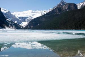 mooie scène met Lake Louise gedeeltelijk bevroren en de bergen eromheen die erop reflecteren. zonnige dag in het voorjaar. banff nationaal park, alberta, canada. foto