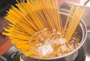 rauwe spaghetti wordt gekookt in kokend water in een keukenpot. gezond italiaans eten en kookconcepten. foto