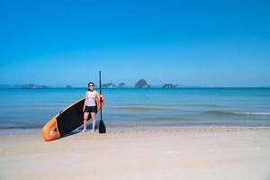 jonge sportieve vrouw die stand-up paddleboard speelt op de blauwe zee op een zonnige dag van de zomervakantie