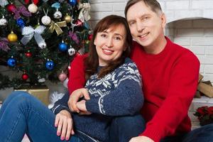 gelukkige paar familie van middelbare leeftijd knuffelen bij de open haard in de buurt van de kerstboom. foto